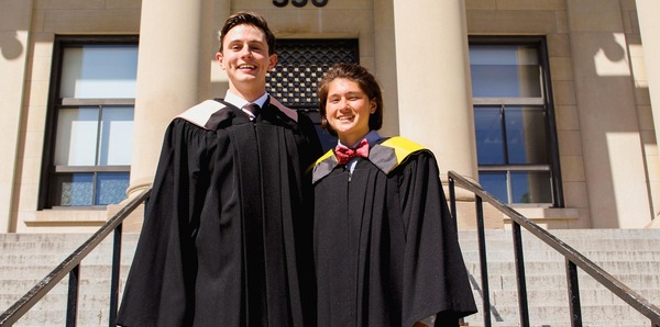 Montana Champagne and Katherine Bearne stand on the steps of Tabaret Hall in convocation robes.