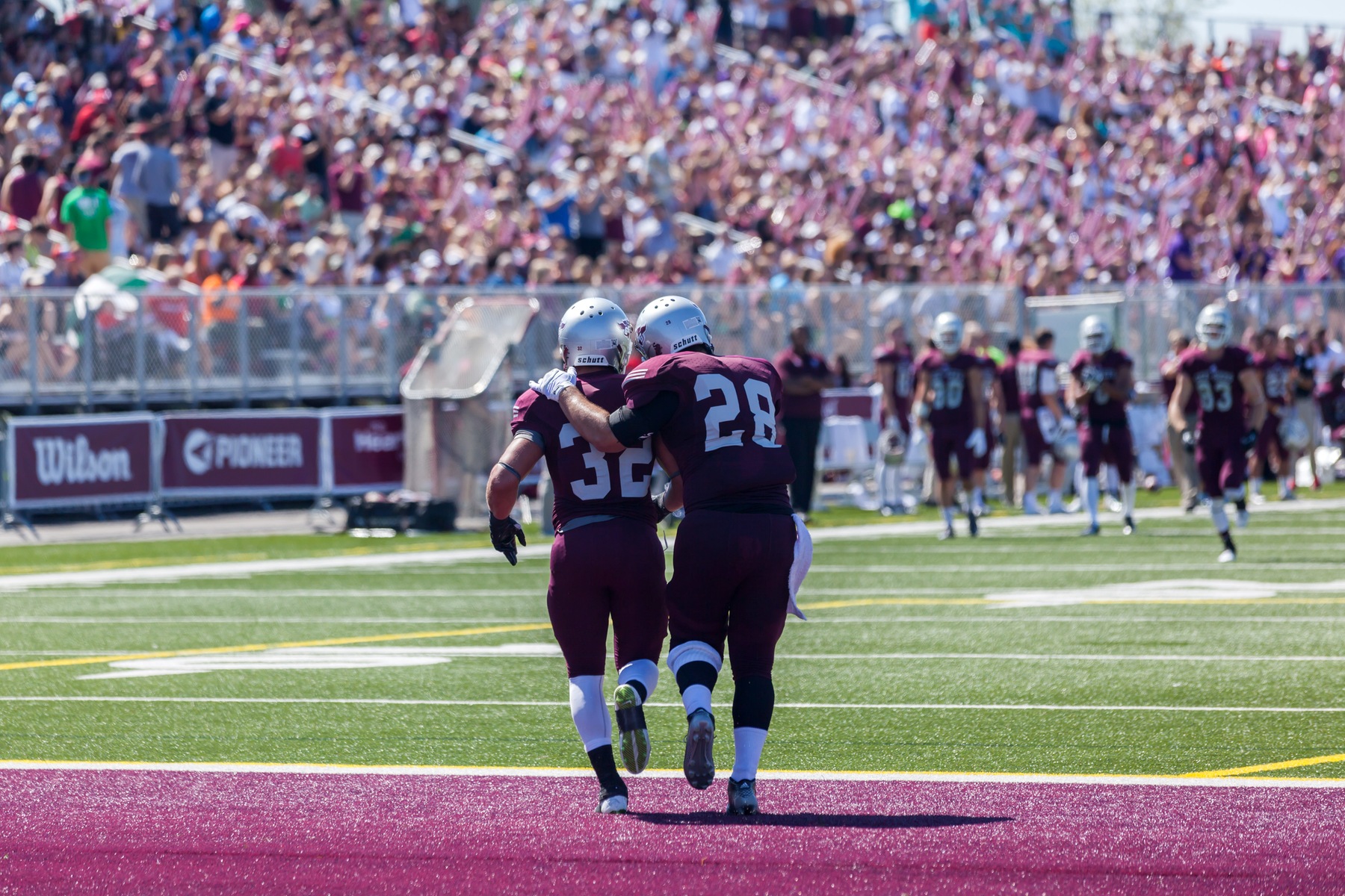 Two football players celebrate in the endzone with grandstand full of fans in the background.