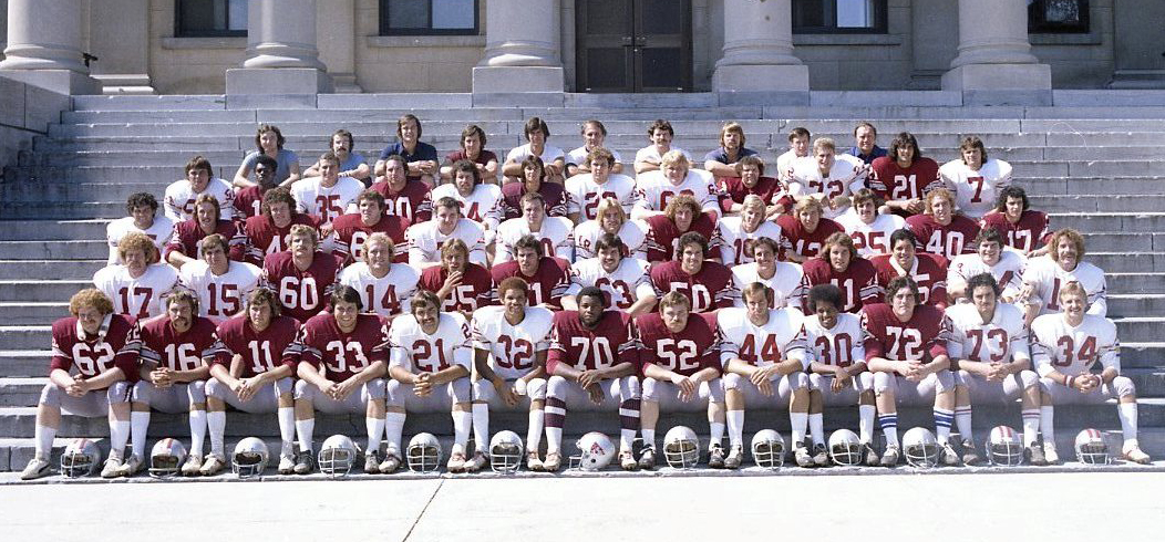 Group photo of football team sitting on steps of Tabaret Hall, wearing garnet and white jerseys.