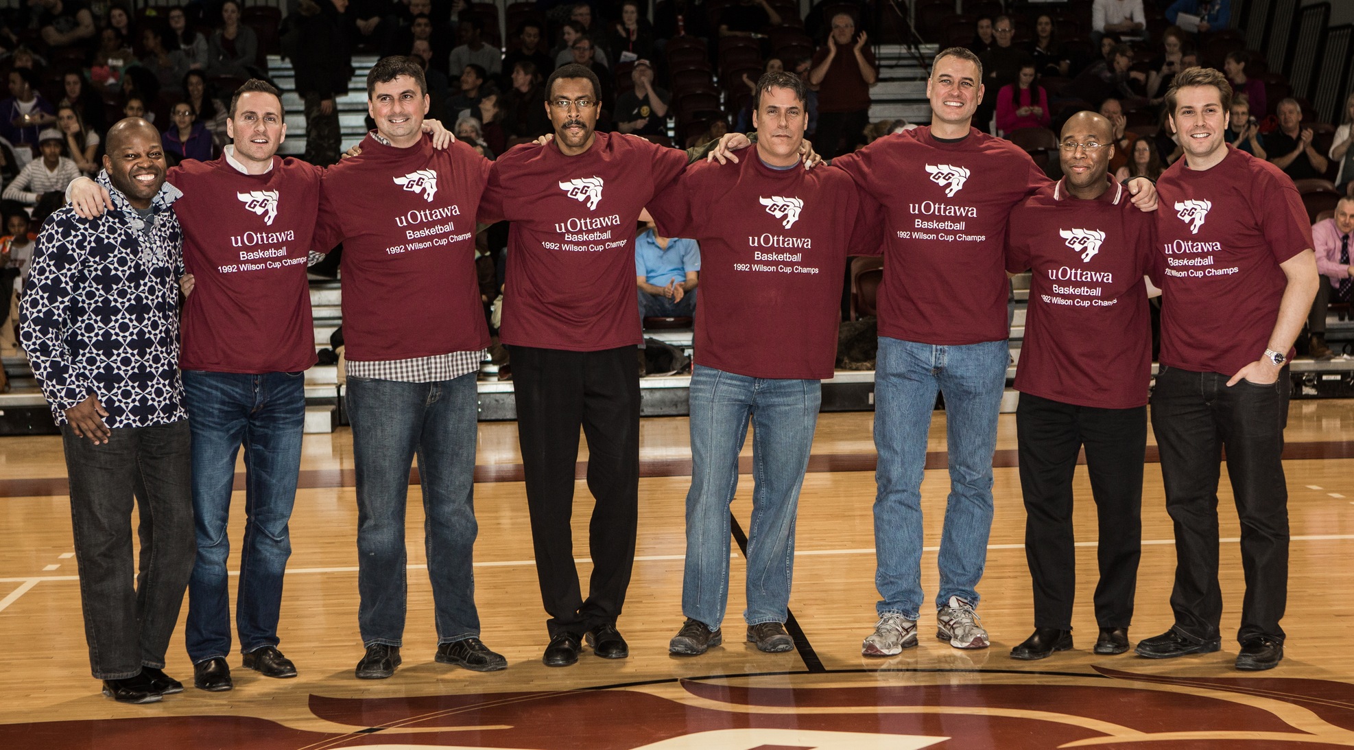 Group photo of basketball alumni on court at Montpetit Hall (eight men in a row).