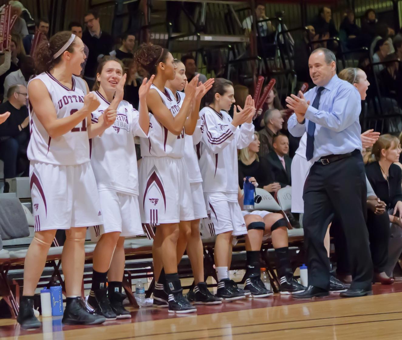 Women's basketball players and Andy Sparks cheering on the bench.