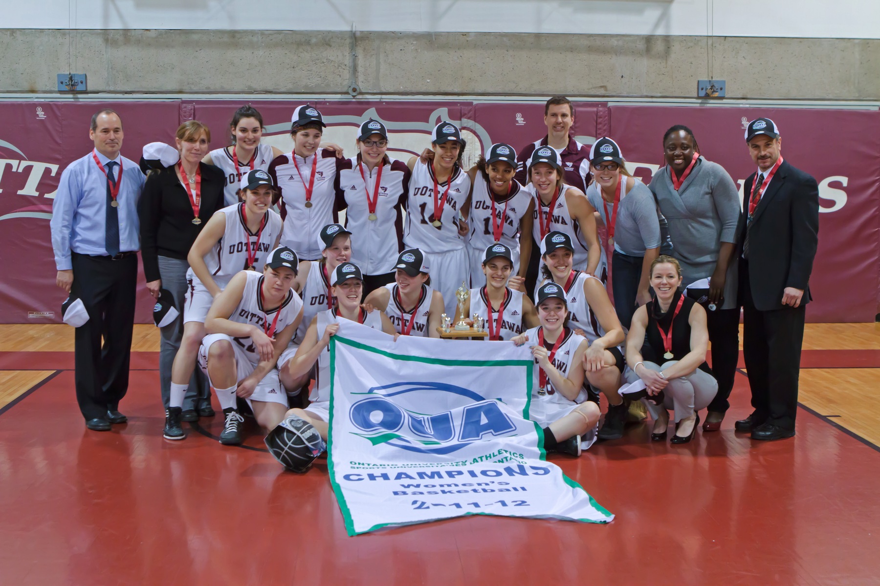 Women's basketball team celebrates with 2012 OUA championship banner at Montpetit Hall.