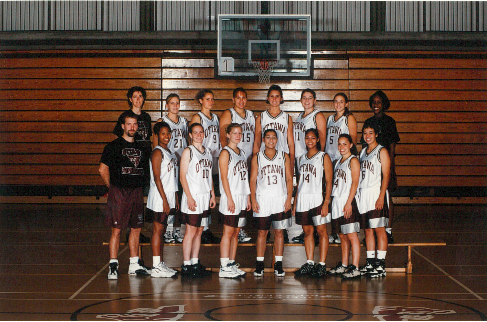 Team photo of women's basketball taken in front of wooden bleachers.