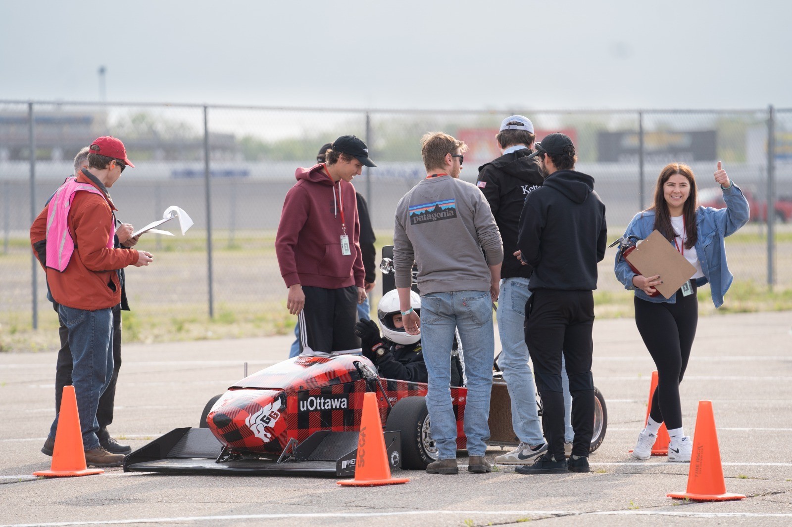 Victoria Hough, right, gives the thumbs up signal and smiles as the uOttawa Formula SAE team inspects its car on the tarmack.