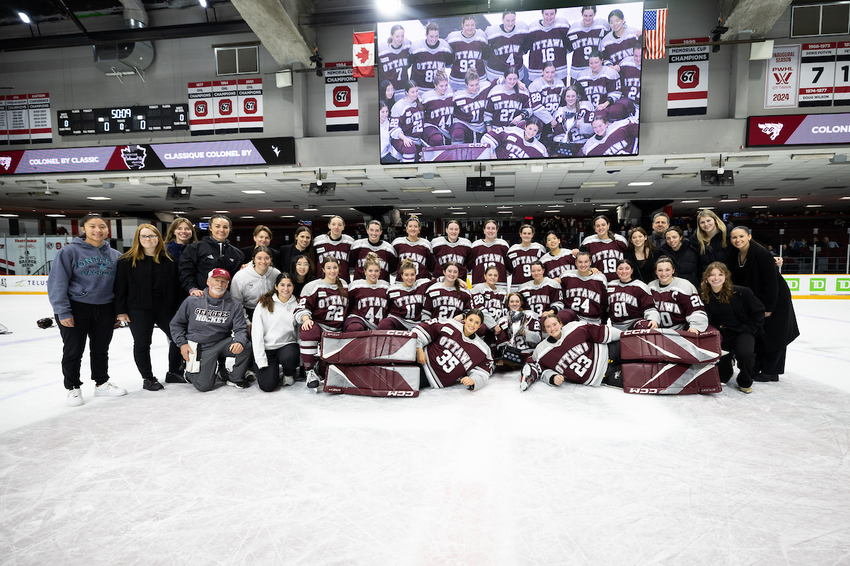 The Gee-Gees women's hockey team players and staff pose for a group photo with the Alerts Cup on the ice at TD Place.