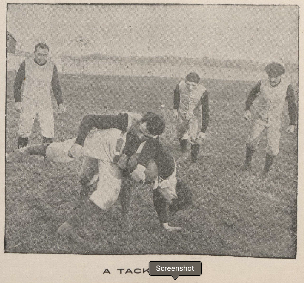 Five men on the football field, one is tackling another while three look on. Text at bottom reads "a tackle."